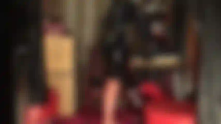 Tenue en latex brillant, bas et masque. La déesse dévoile ses courbes dans un latex moulant, des bas transparents à coutures et une jupe crayon noire avec des gants. La tenue est complétée par un masque en latex.