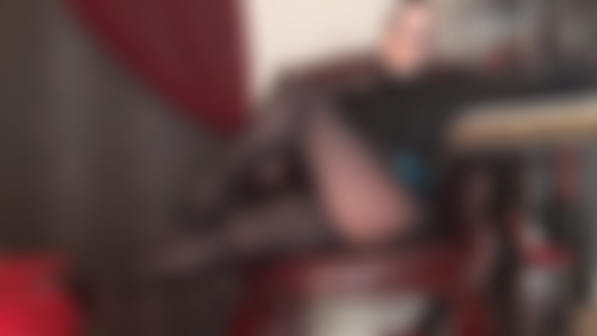 Maîtresse séduit avec ses jambes en collants noirs brillants et un décolleté sexy en soutien-gorge en dentelle.