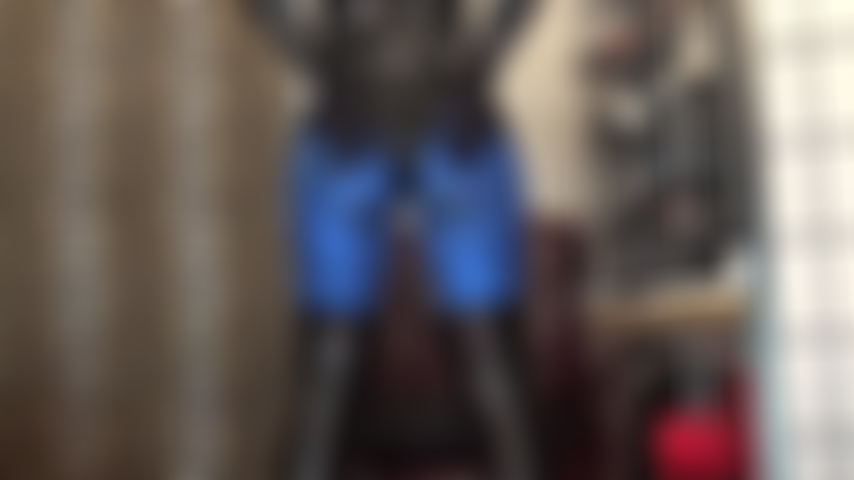 Cul en leggings lycra métallisé bleu et body en pvc brillant, pieds en collants marron foncé.
