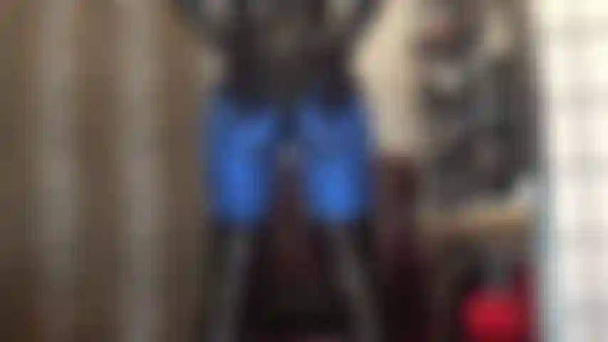 Cul en leggings lycra métallisé bleu et body en pvc brillant, pieds en collants marron foncé.