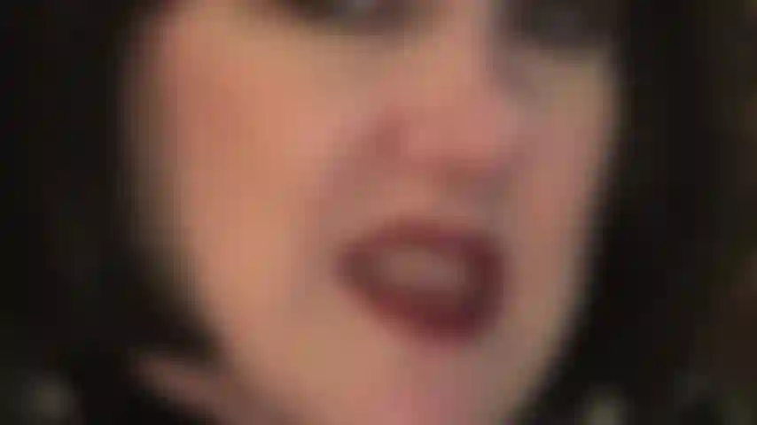 Gros plan du visage avec une perruque noire au carré, taquinant avec des lèvres rouges à lèvres et une langue humide ainsi que des dents et des mains gantées de cuir qui aimeraient tenir vos couilles.