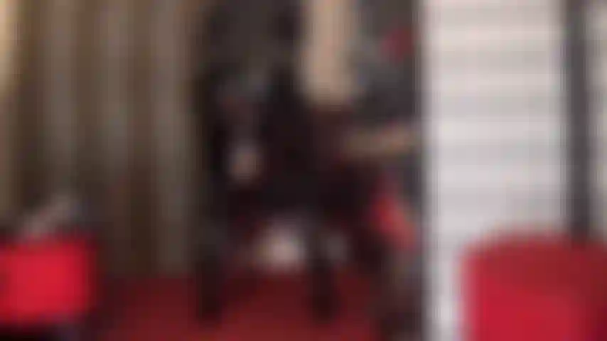 Une déesse en pvc en combinaison noire brillante qui taquine avec son énorme bite blanche à sangle qui dépasse de sous sa couche de jupe.