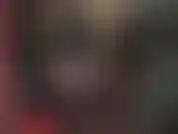 Maîtresse coquine en latex avec capuche, gants, bottes et gros strapon blanc.