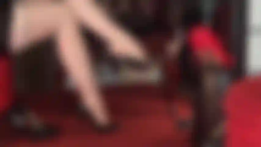 Des collants nude à motifs jarretelles et coutures, des jambes croisées et des pieds séduisants sur lesquels pendent différentes paires d'escarpins classiques.