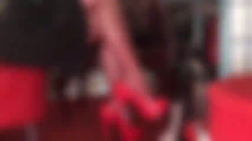 Des jambes croisées séduisantes dans des collants rouges et des escarpins rouges brillants taquinent la bite douloureuse de l'esclave.