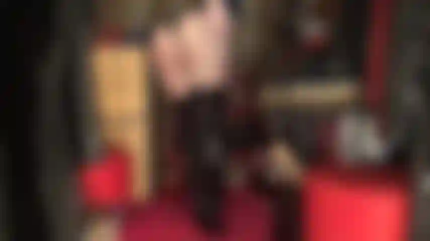 Une déesse adorant le cul dans un body string en pvc noir brillant et des bottes hautes sur des collants noirs transparents.