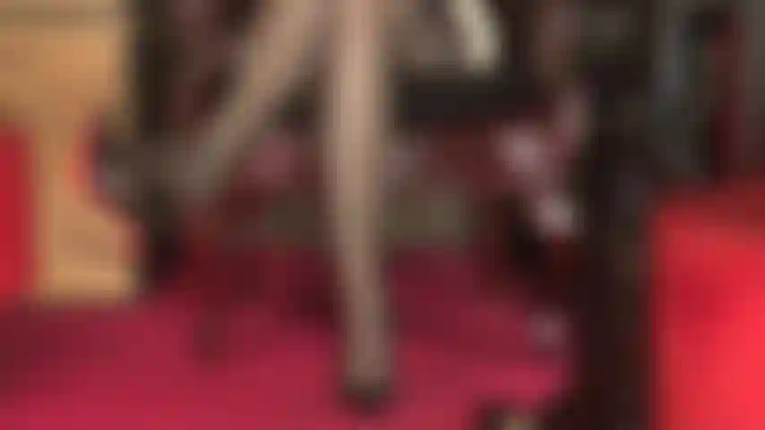 Une vue sexy sur des jambes vêtues de bas, une ceinture porte-jarretelles à plusieurs sangles qui dépasse, des cuisses croisées sexy et des orteils qui pendent une pompe à semelle rouge.