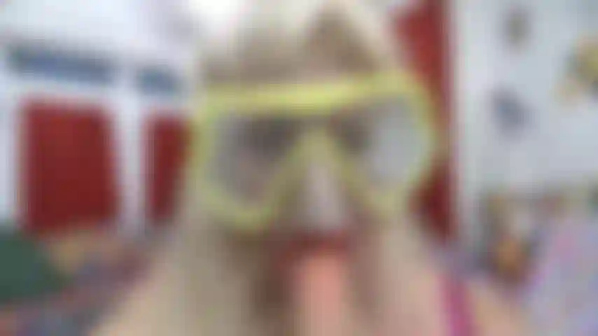 Point de vue du visage dans un masque de plongée l'embuant avec du rouge à lèvres rouge en suçant un jouet blanc.